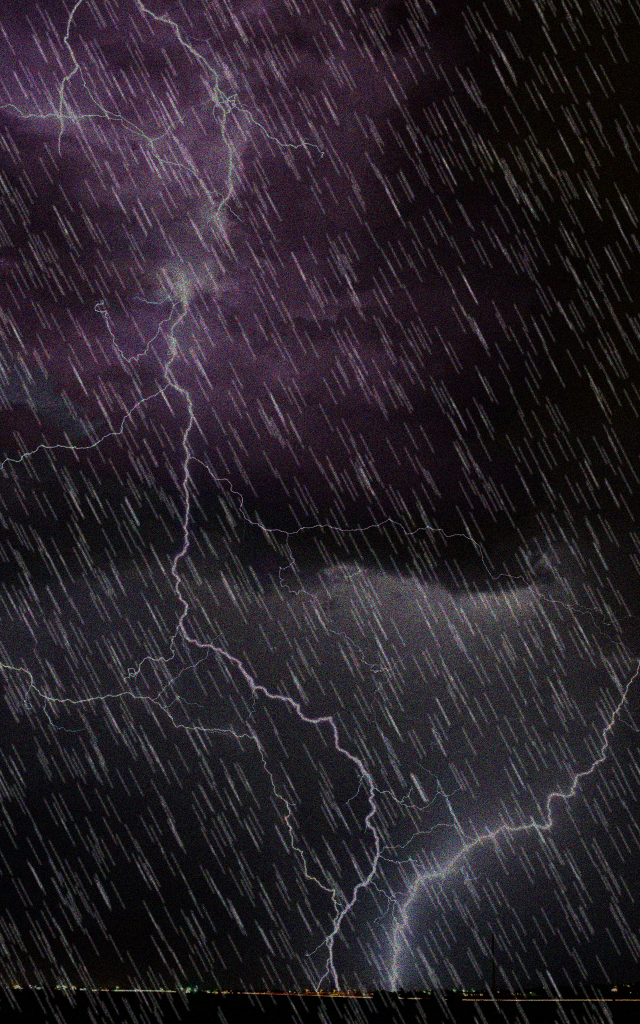 Degraded input: a lightning storm shot through heavy rain streaks and sensor noise.